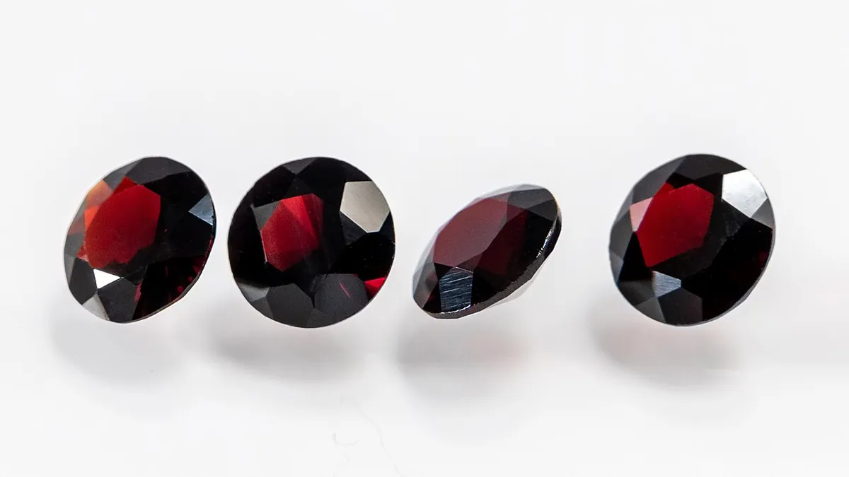 Four round faceted dark red garnets in a row on a white background