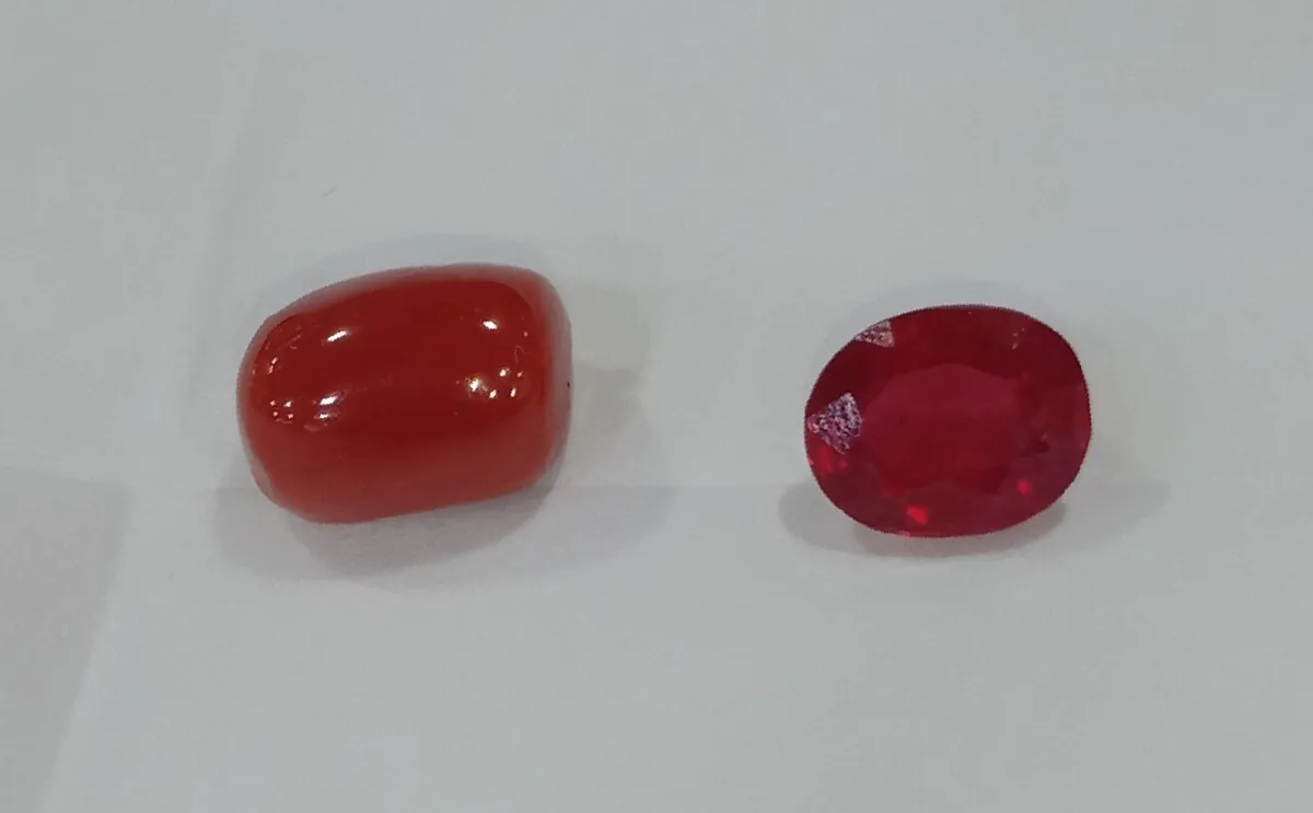 Polished red coral bead beside a faceted oval ruby on a light gray background